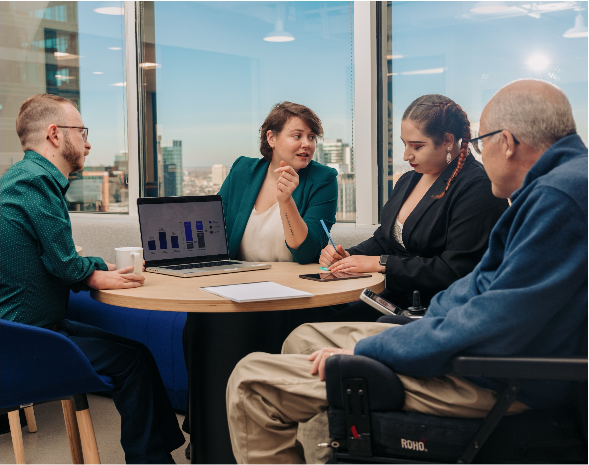 A person in a wheelchair collaborating with several others who are all sitting  around a small conference table.