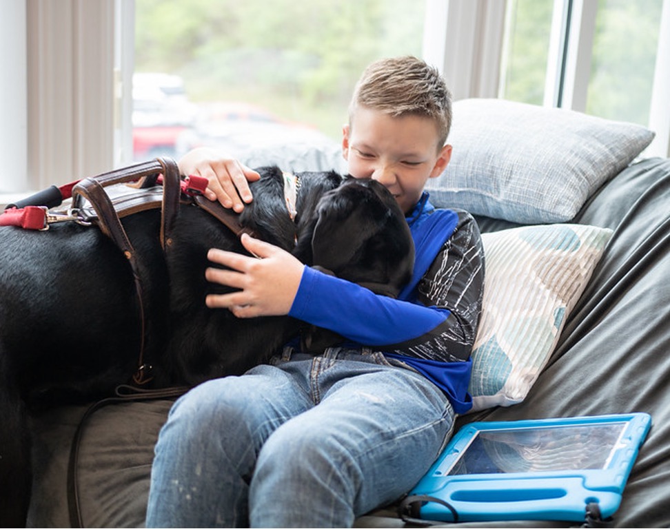 A young boy puts down his tablet to hug his service animal.